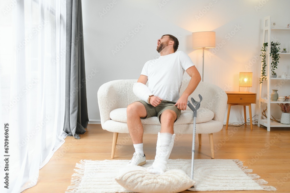 Recovery after physical injury in accident at home: Sad unlucky young man with broken leg, injured arm Recovery after physical injury in accident at home: Sad unlucky young man with broken leg, injured arm