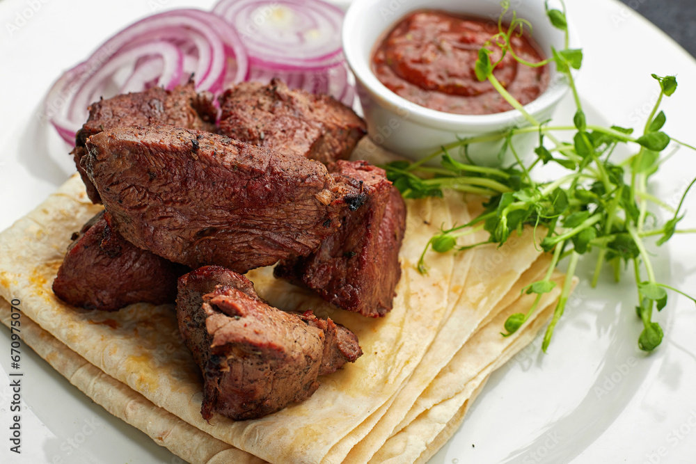 Fried shish kebab with lavash, sauce, microgreen and onion, on a white plate, on a gray background Fried shish kebab with lavash, sauce, microgreen and onion, on a white plate, on a gray background