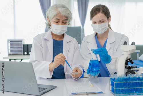 Beautiful young female scientist and two elderly women work in a laboratory with test tubes researching blue chemicals in the healthcare industry.