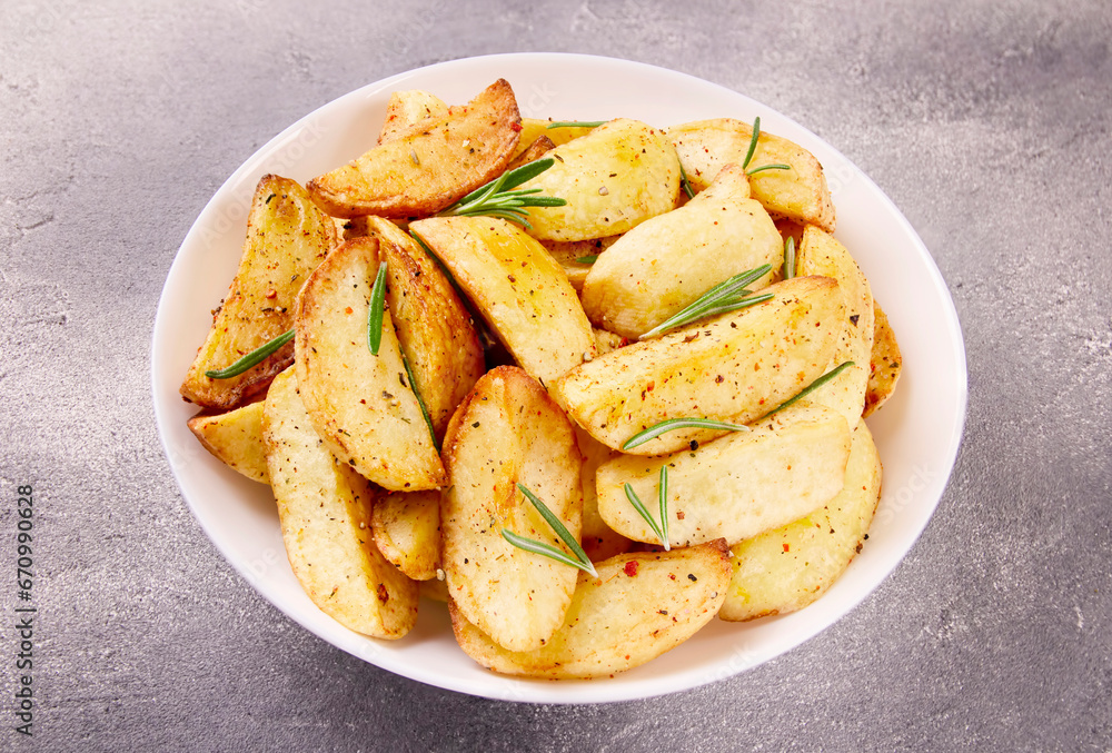 Baked potato wedges with seasonings on a plate on a gray stone.