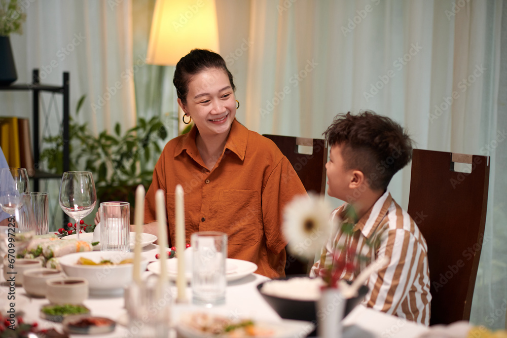 Smiling mother taking to her kid when sitting at dinner table at family celebration Smiling mother taking to her kid when sitting at dinner table at family celebration