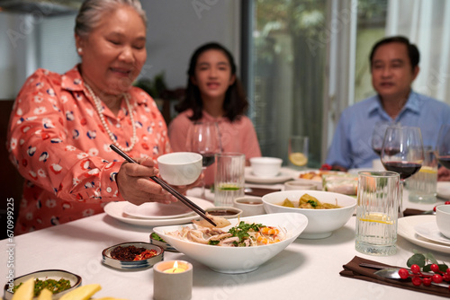 Grandmother taking some food from dish at family dinner table