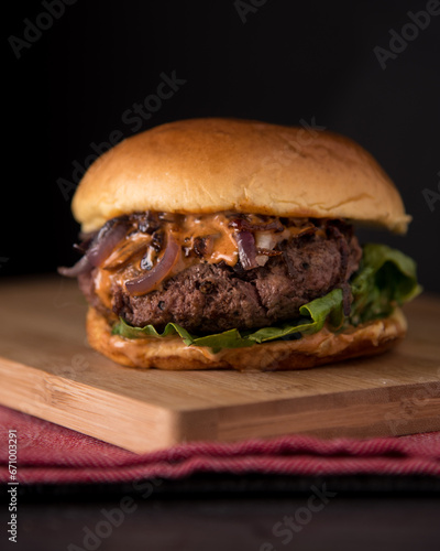 Juicy Homemade burger with lettuce onions, and chipotle sauce in a brioche bun. Dark and moody background.