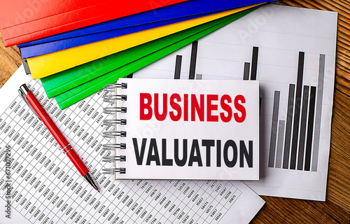BUSINESS VALUATION text on a notebook with pen, folder on a chart background