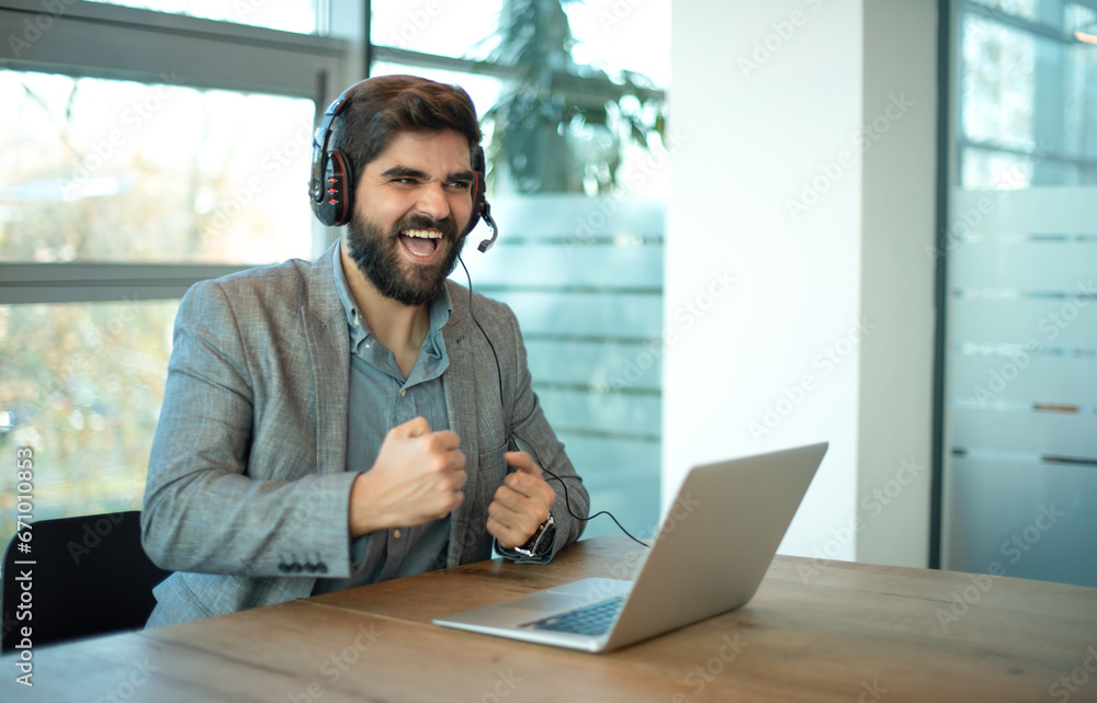 Cheerful businessman with clenched fists using laptop in office. Successful businessman entrepreneur in formal suit holding fists up celebrating important job agreement with customer deal done. Cheerful businessman with clenched fists using laptop in office. Successful businessman entrepreneur in formal suit holding fists up celebrating important job agreement with customer deal done.