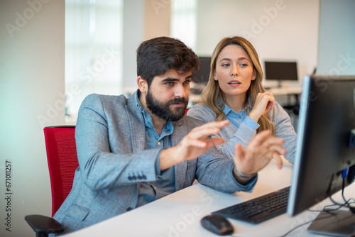 Two diverse businesspeople chatting sitting behind computer in office.Bearded businessman sharing ideas or startup business plan with female coworker.