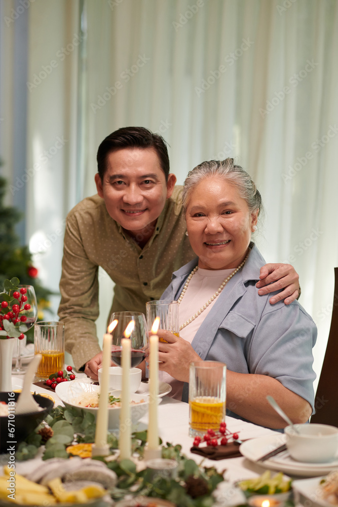 Portrait of cheerful mother and her adult son at Christmas dinner table