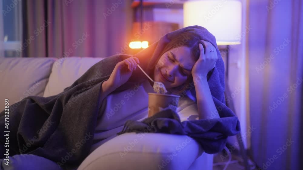 Portrait of sad young woman dealing with stress by eating food sitting on couch at home Upset brunette female wrapped in blanket crying and eating ice cream indoors at late night Mental heath problem Portrait of sad young woman dealing with stress by eating food sitting on couch at home Upset brunette female wrapped in blanket crying and eating ice cream indoors at late night Mental heath problem