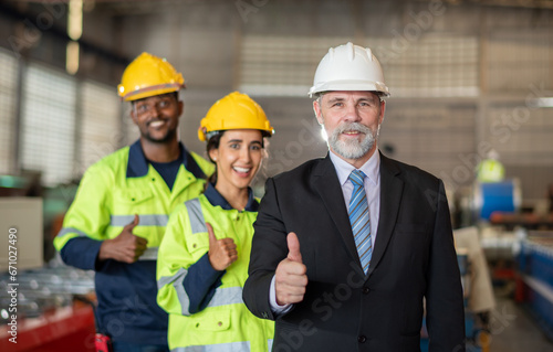 mature older boss engineer with beard mustache on face wear helmet standing smile and hand show good thumb at construction factory site with worker leader team for happy working in factory site.