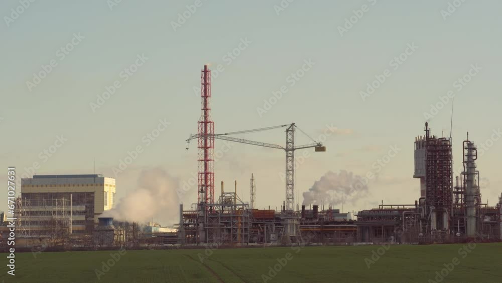 A view of a large factory or enterprise with large smoking chimneys against a blue sky. Environmental pollution by industrial waste. White smoke comes out of the chimney. A view of a large factory or enterprise with large smoking chimneys against a blue sky. Environmental pollution by industrial waste. White smoke comes out of the chimney.