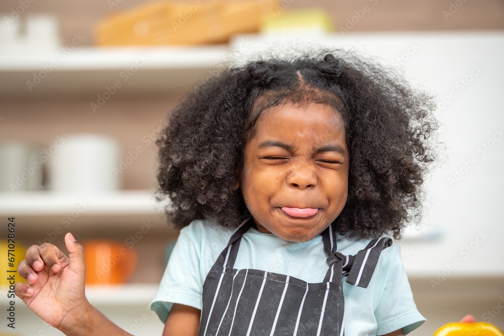 Fototapeta premium african afro hair black kid Cute taste oranges citrus sour flavour on ripe mouth in kitchen. candid back african daughter kid afro hair frowning face in taste feelings mood sour with sliced oranges.