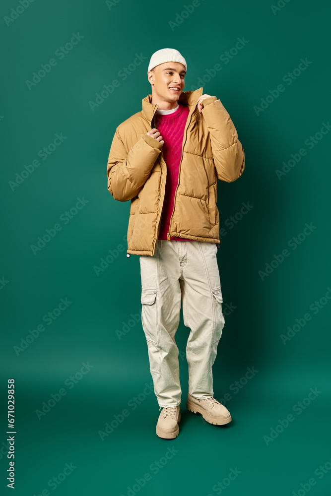 happy young man in beanie hat and stylish puffer jacket on turquoise background, winter trends happy young man in beanie hat and stylish puffer jacket on turquoise background, winter trends