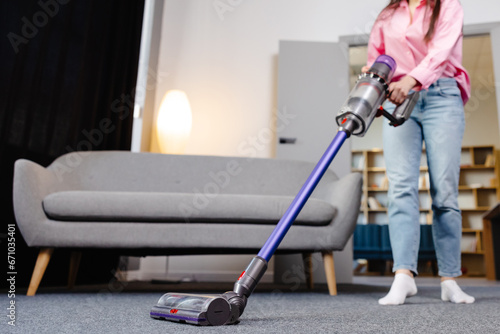 Tableau sur toile Young woman uses cordless vacuum cleaner to clean home carpet