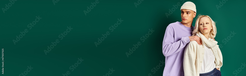 young man in beanie hat and winter attire touching shoulders of blonde woman on turquoise, banner young man in beanie hat and winter attire touching shoulders of blonde woman on turquoise, banner