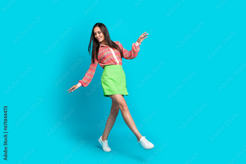 Full length photo of beautiful charming woman looking down when she steps in her stylish summer outfit isolated on cyan color background