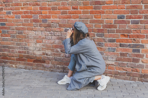 Young millennial woman takes picture in front of brick wall in city street - photographer and vintage camera hobby concept