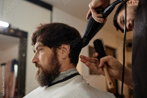 Bearded young man making a new haircut in barber shop