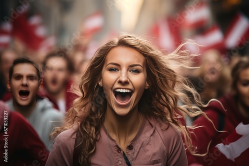 Young cheerful girl against the backdrop of crowd of young people marching along city street under red and white flags. Poland Independence Day. Patriotic concept with national state symbol.