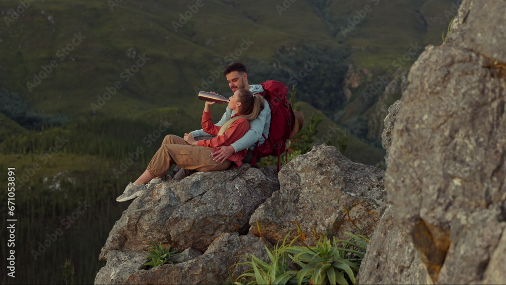 Hiking, mountain and drinking water, couple relax on outdoor adventure and peace in nature with romance. Trekking, rock climbing and love, man and woman with view of natural cliff with sharing drink.