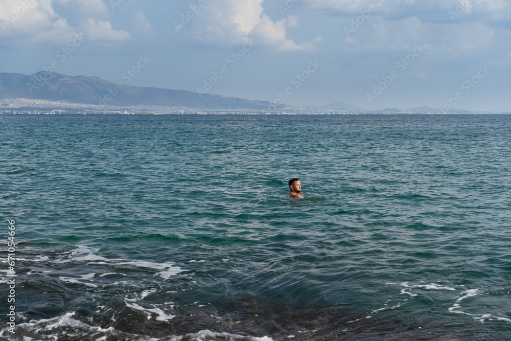 A man with a beard swims in the sea near Athens.