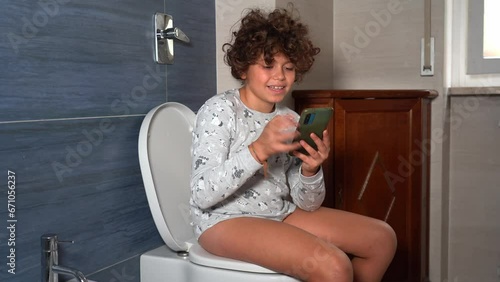 9 year old boy goes to the bathroom on the toilet looking at the smart phone - addiction to social networks and the internet - spending too much time online during daily life 