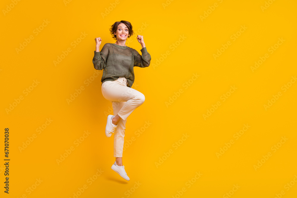 Photo of excited cheerful cool girl dressed stylish clothes celebrate success jumping up empty space isolated on yellow color background