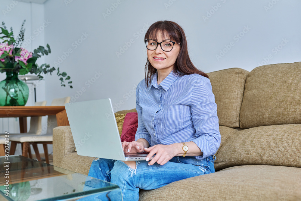 Portrait of middle-aged woman with laptop on sofa in living room Portrait of middle-aged woman with laptop on sofa in living room