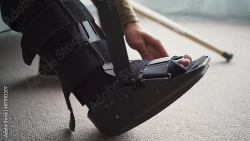 Young man with leg injury using Splint, walker boot, Orthosis. Guy with sprained ankle at home photo