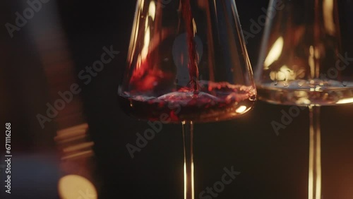 Red wine being poured into a wine glass with beautiful mountains at sunset background. Romantic dinner with wine and food by the vineyards. Close-up shot of wine bottle pouring deep red wine, creating
