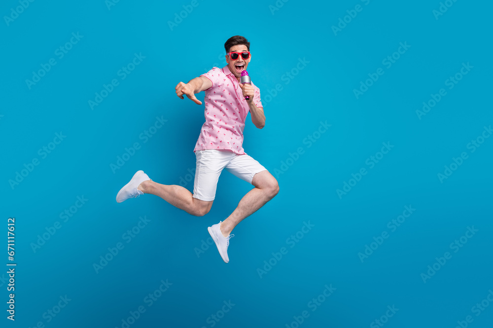 Full length photo of overjoyed nice person jump sing microphone empty space isolated on blue color background