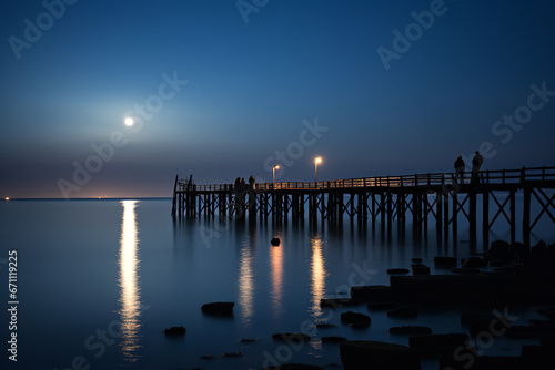 Against the gentle lull of waves  fishermen on a timeworn pier harness the moon s radiant glow tradition with nature s rhythm.