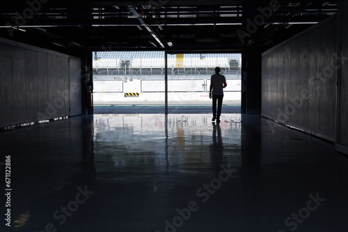 Silhouettes of a man entering a race car racing circuit paddock.