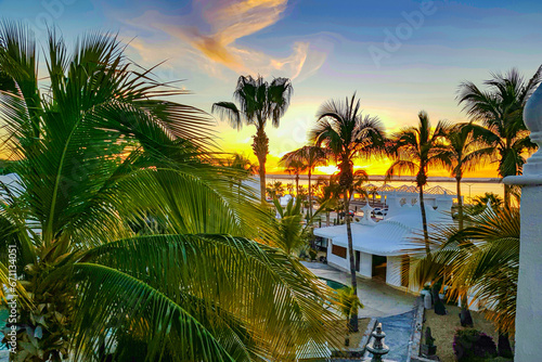 Coastal sunset seen from a terrace  palm trees against reddish blue and orange sky  sun beginning to set in background  calm day in La Paz  Baja California Sur Mexico