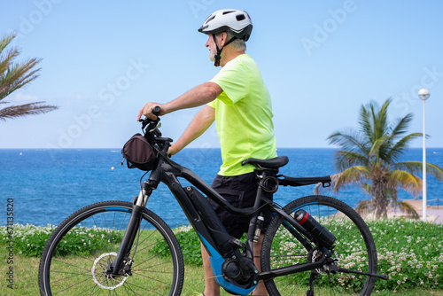 Elderly athletic man with electric bicycle in outdoors excursion at sea. Senior man in helmet enjoying freedom and healthy lifestyle