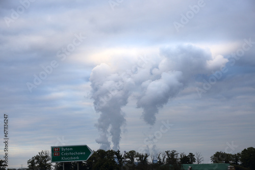 Ogromne kłęby dymu z kominów elektrowni oświetlone przez słońce nad chmurami.