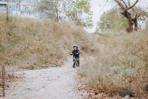 Happy child, little preschool boy rides a balance bike, a bicycle without wheels on a road with a slope outdoors in autumn. Photography, portrait, childhood concept, sports.