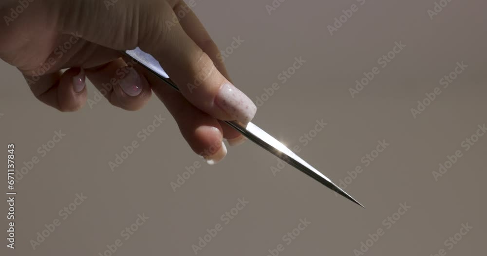 female hand holding tweezers on gray background. professional eyelash extension female hand holding tweezers on gray background. professional eyelash extension