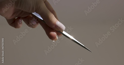 female hand holding tweezers on gray background. professional eyelash extension