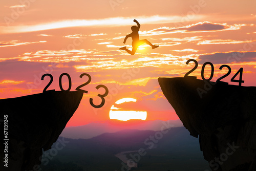 Greetings and have a great Christmas and new year in 2024.silhouette of a man leaping from a cliff in 2023 to one in 2024 under a cloudy and sunny sky. photo