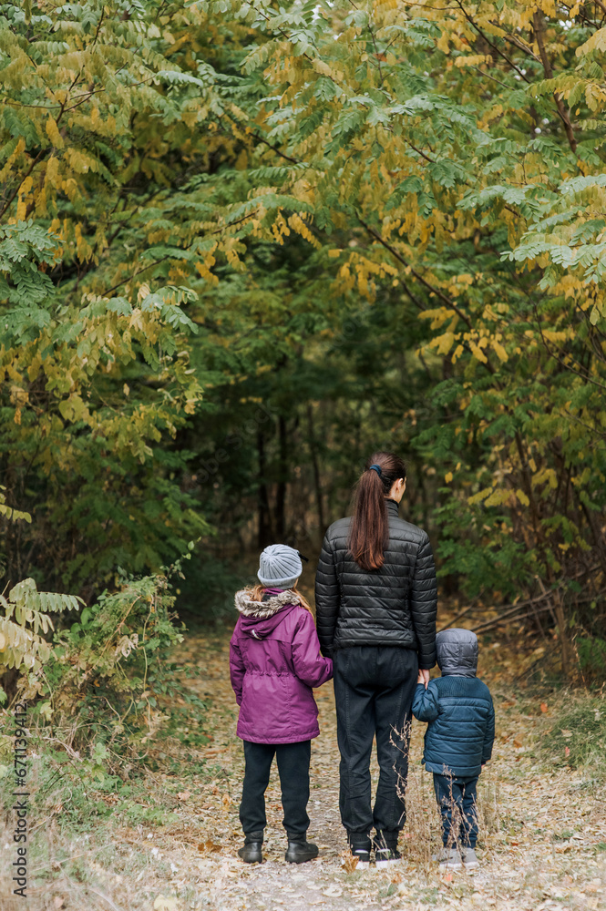 A family, a mother with her son and daughter, are walking through the forest in an outdoor park, holding hands. Photography, portrait. A family, a mother with her son and daughter, are walking through the forest in an outdoor park, holding hands. Photography, portrait.