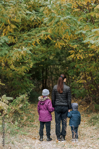 A family, a mother with her son and daughter, are walking through the forest in an outdoor park, holding hands. Photography, portrait.