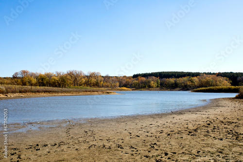 Fototapeta Naklejka Na Ścianę i Meble -  Iowa beach landscape with sand in the foreground, a lake in the middle, and fall trees in the background. 