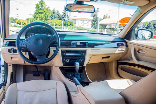 Beige interior with a black car steering wheel from the inside against the background of the road