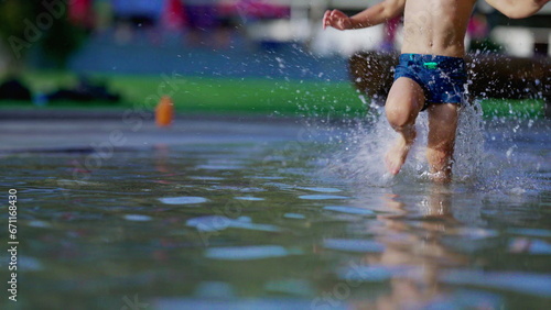Joyful child running in swimming pool water splashing water in slow-motion during summer day. Active little boy sprinting at 120fps photo