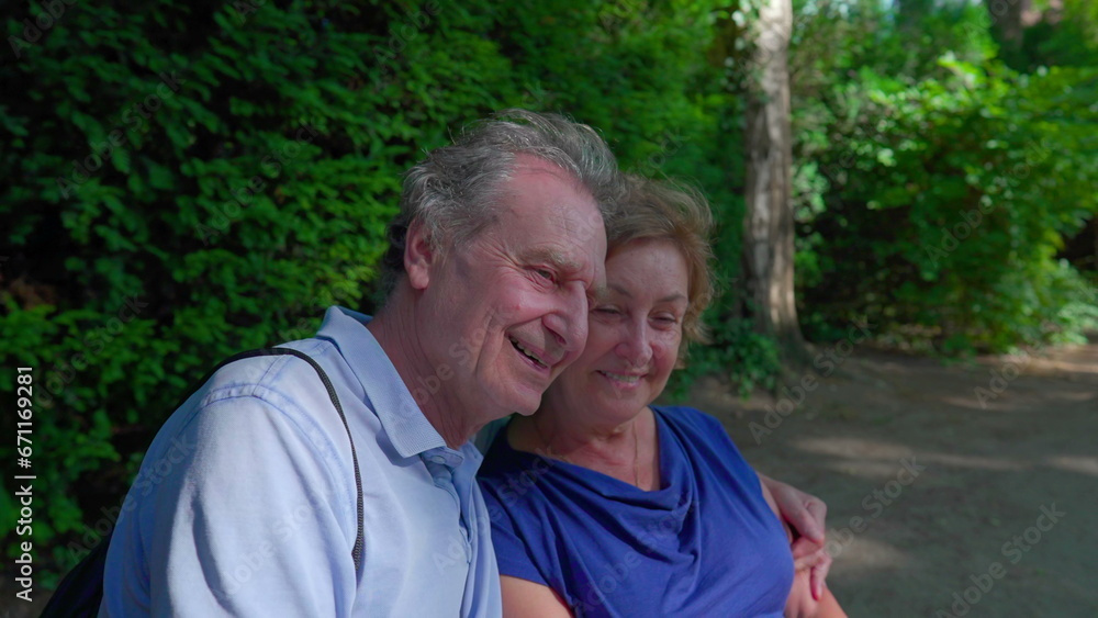 Joyful senior couple enjoying sunny day at park bench. Husband putting arm around elderly wife smiling and laughing in outdoor, happy marriage Joyful senior couple enjoying sunny day at park bench. Husband putting arm around elderly wife smiling and laughing in outdoor, happy marriage