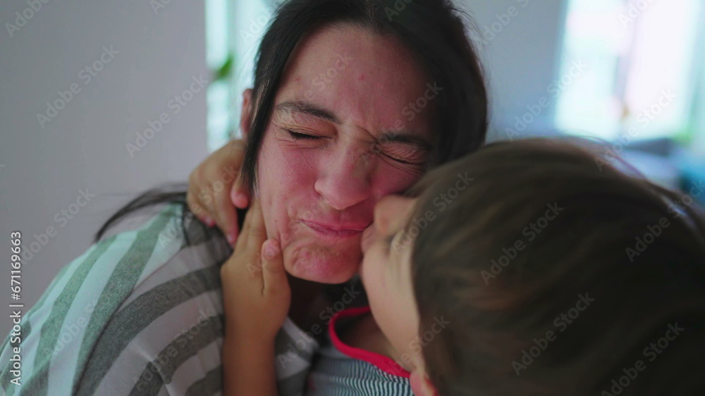 Energetic child kissing mother in cheek with rough embrace. Excited son warm loving embrace kisses mom energetically Energetic child kissing mother in cheek with rough embrace. Excited son warm loving embrace kisses mom energetically