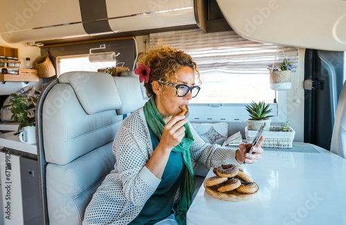 One woman eating dognuts donuts inside a modern luxury camper van. People and unhealthy sugar food. Adult female using phone in indoor leisure activity inside motorhome rv vehicle alone photo