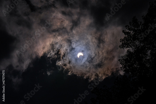 wide angle of partial solar eclipse in sky lighting up clouds all around with sky dark. 