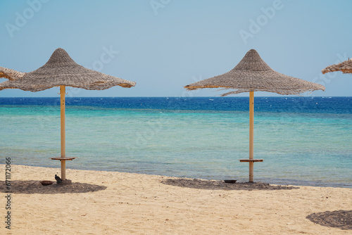 Straw sun umbrellas or parasols on empty beach near sea, sunny day