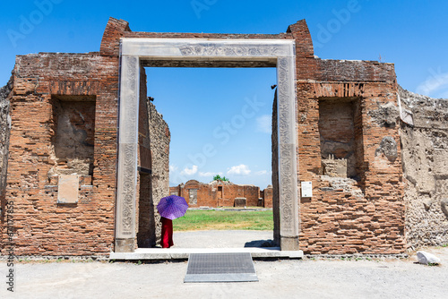 Woman in red dress protecting herself from the heat with an umbrella while visiting archaeological excavations. Summer tourism, heat, Italian archaeological site.
